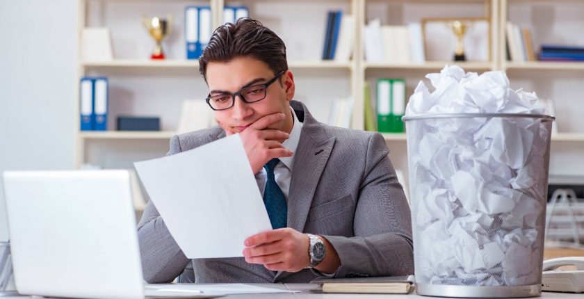 Businessman looking at executive CV with recycling bin next to him